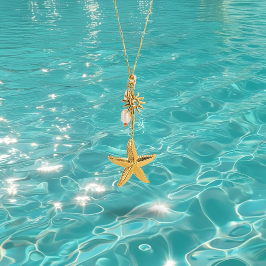 Collier doré Bahari avec pendentifs étoile de mer, soleil et perle, photographié devant la mer